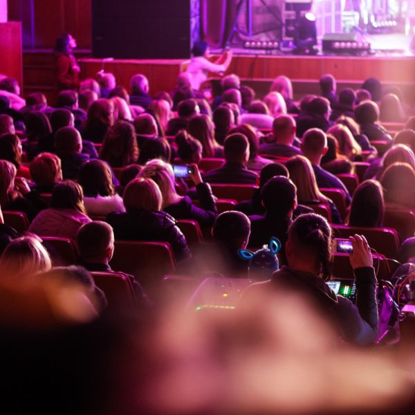 Defocused spectators sit in the hall and watch a concert. People in the auditorium watching the performance. Theater audience. Out of focus