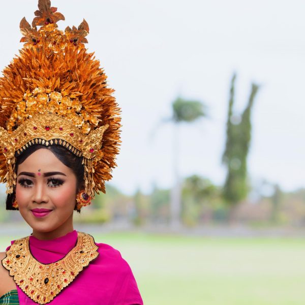 Denpasar, Bali island, Indonesia - June 23, 2018: Face portrait of beautiful young woman in traditional Balinese dance costume with golden headdress on street parade at art and culture festival.