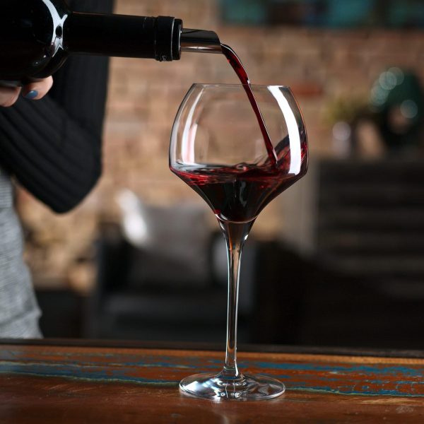 Elegant woman pouring red wine from wine bottle to wine glass at home in a cosy dark room.