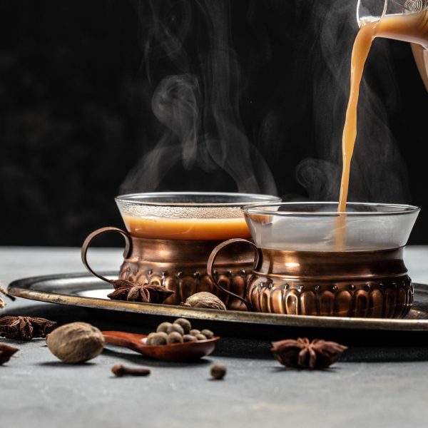 Indian masala chai tea. Hot masala chai spiced tea with milk and spices is poured into a glass glass on dark background. Long banner format. place for text.
