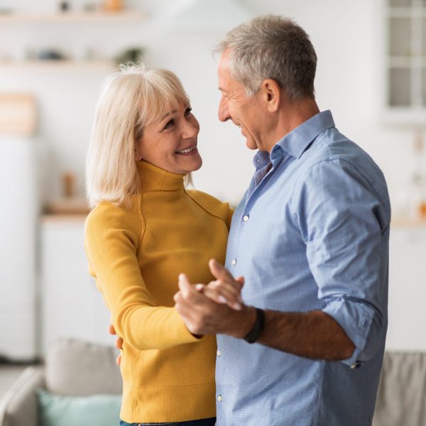 Loving Senior Couple Dancing At Home Holding Hands Having Date