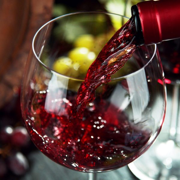 Macro shot of pouring red wine into glass. Still life with grapes of wine served on dark stone table.